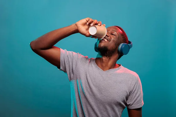 Nadšený muž pije kávu z poháru a nosí sluchátka — Stock fotografie