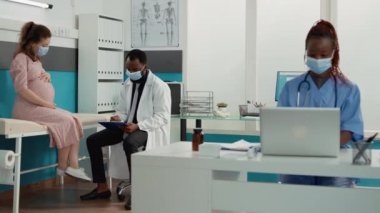 Afrikalı Amerikalı sıhhiyeci hamilelik karnı olan hastayı muayene ediyor.