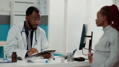 Genç doktor, beklenen kadınla istişare üzerine tablet yazıyor.