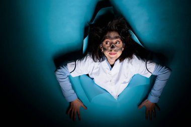 Aptal yüz ifadesi ve tuhaf görünüşü olan çılgın bir biyokimya uzmanı mavi arka plandayken tuhaf davranıyor..