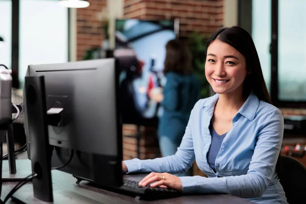 Smiling company employee sitting at desk in office workspace while looking at camera. — Stock Photo, Image
