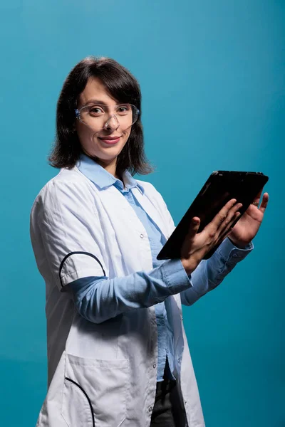 Позитивний фахівець з усміхненої хімії, що має сучасну таблетку, що стоїть на синьому фоні — стокове фото