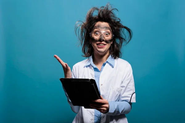Científico loco con la cara sucia y el peinado desordenado que tiene tableta de pantalla táctil actuando sorprendido y loco —  Fotos de Stock