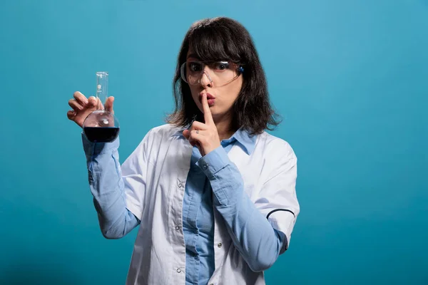 Professionele biochemicus die Erlenmeyer glazen pot vasthoudt terwijl hij zwijggebaar maakt op een blauwe achtergrond. — Stockfoto