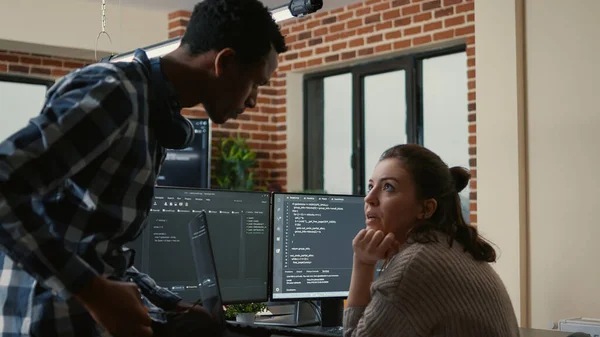 Junior developer sitting down on desk showing laptop with source code to senior dev — Photo