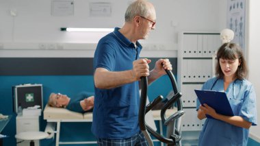 Yaşlı bir hastanın fiziksel egzersiz yapmasına yardımcı olan hemşire.