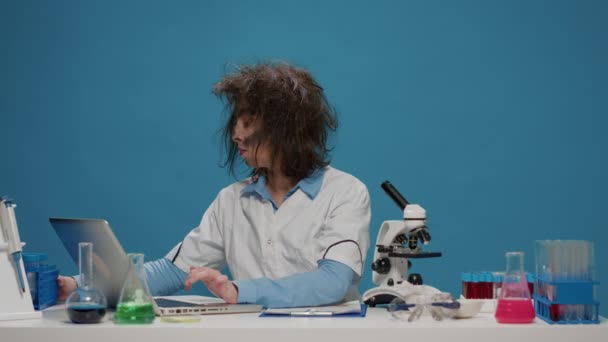 Legrační šílený ženský vědec při pohledu na zkumavky na stole — Stock video