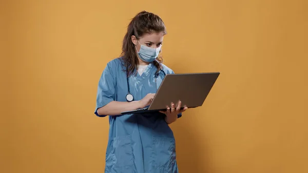 Doctor with stethoscope holding laptop and typing on keyboard looking at screen — 스톡 사진