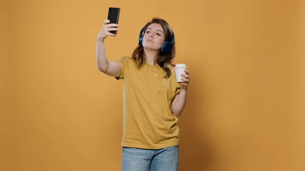 Kablosuz kulaklıkla müzik dinlerken bir fincan kahve içerken selfie çeken rahatlatıcı kadının portresi. — Stok fotoğraf