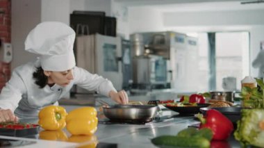 Kadın aşçı tavaya rendelenmiş peynir ekliyor.