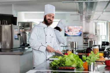 Gastronomi uzmanı taze malzemeler kullanarak lezzetli organik yiyecekler pişirirken kameraya kendinden emin bir şekilde gülümsüyor..
