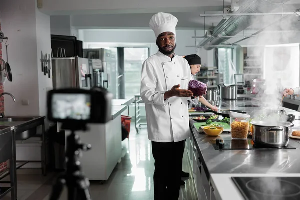 African American επικεφαλής σεφ έχουν κόκκινο λάχανο κινηματογράφηση μαγείρεμα γκουρμέ πιάτο, ενώ κοιτάζοντας κάμερα. — Φωτογραφία Αρχείου