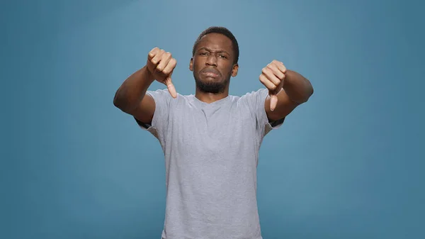 Disappointed person showing thumbs down symbol in studio — ストック写真