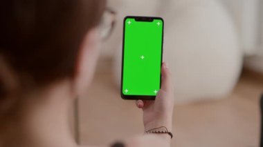 Yeşil ekranlı dikey akıllı telefonu olan genç bir kadının çevrimiçi video içeriği veya web sitesi içeriğini izlediği aşırı yakın plan