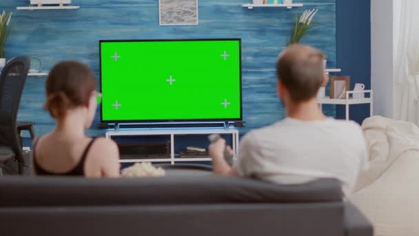 Couple sharing a bowl of popcorn while watching tv and switching channels looking at green screen — Vídeo de stock