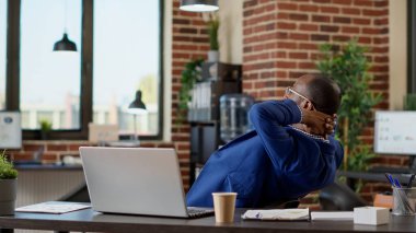 Proje yöneticisi dizüstü bilgisayarla online şirkete ara veriyor, elleri başının arkasında oturuyor. Stres atmak için ara vermek, huzur içinde tatmin olmak. Üçayak atışı.