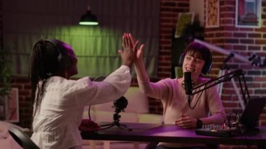 Online radio host doing high five hand gesture with african american influencer during live podcast in living room
