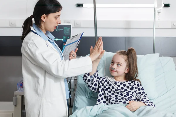 Hospital pediatrician specialist high-fiving sick little girl while in patient treatment ward room. — Stock Photo, Image