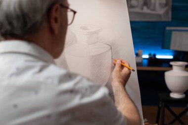 Resim sehpasındaki kağıt brandaya kalem çizen yaratıcı yaşlı adamın yakın çekimi.