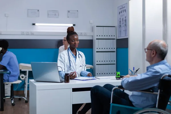 Healthcare clinic medic expert conversating with sick senior patient in wheelchair about illness — Stockfoto