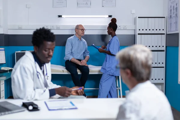Hospital nurse conversating with senior man about consultation results — Zdjęcie stockowe
