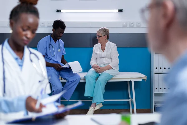 Hospital nurse conversating with sick retired woman about illness diagnostic and health risks. — Stockfoto