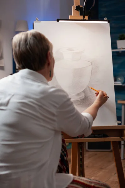 Portrait of elderly artist sketching still life using sharp pencil on paper sketching vase model — Fotografia de Stock