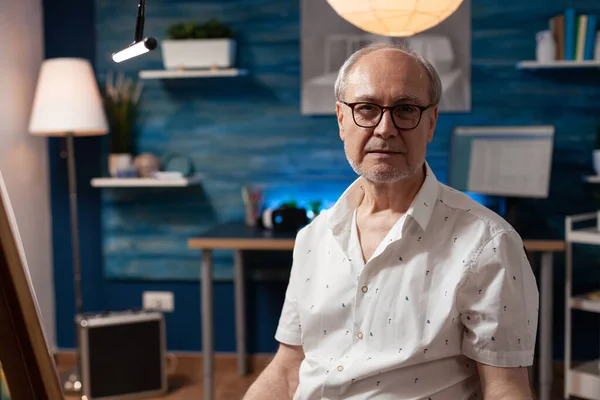 Closeup of senior man with glasses posing confident with masterpiece sitting in professional creative studio — Stock Photo, Image