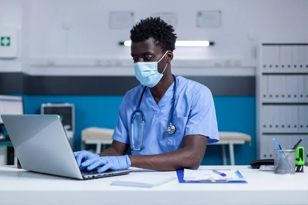 Infirmière portant un masque lors de l'utilisation d'un ordinateur portable pour analyser les documents du patient — Photo