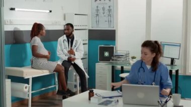 Hamilelik karnı olan kadın muayenede doktorla konuşuyor.