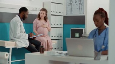 Afrikalı Amerikalı doktor hamile kadına yatakta danışmanlık yapıyor.