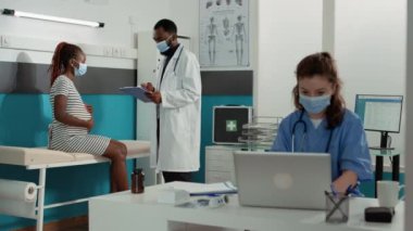 Yüz maskeli hamile kadın ve doktor danışmanlık yapıyor.