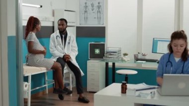 Afrikalı Amerikalı doktor ve hamile hasta kabinede toplanıyor.