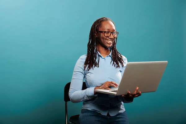 Χαρούμενη όμορφη κυρία με φορητό σύγχρονο υπολογιστή στέκεται σε μπλε φόντο, ενώ σερφάρετε πρόγραμμα περιήγησης. — Φωτογραφία Αρχείου