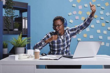 Karaoke yaparken kablosuz kulaklık takan heyecanlı Afro-Amerikan ofis çalışanı.