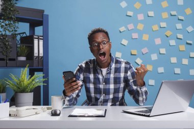 Şirket ofisinin neşeli çalışanı cep telefonuyla oyun oynarken masada oturuyor..