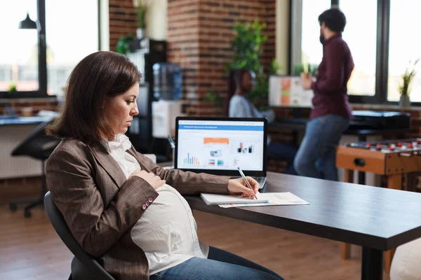 Mulher grávida analisando o crescimento econômico da empresa e revisa gráfico financeiro e de gestão. — Fotografia de Stock