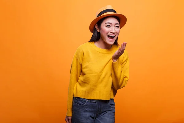 Portrait de heureuse femme asiatique positive riant chaleureusement tout en portant des vêtements jaunes sur fond orange. — Photo