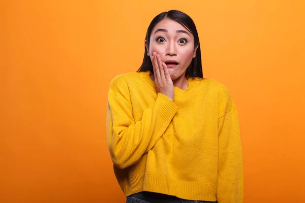 Concerned troubled asian woman wearing yellow vibrant sweater while putting hand on face. — Photo