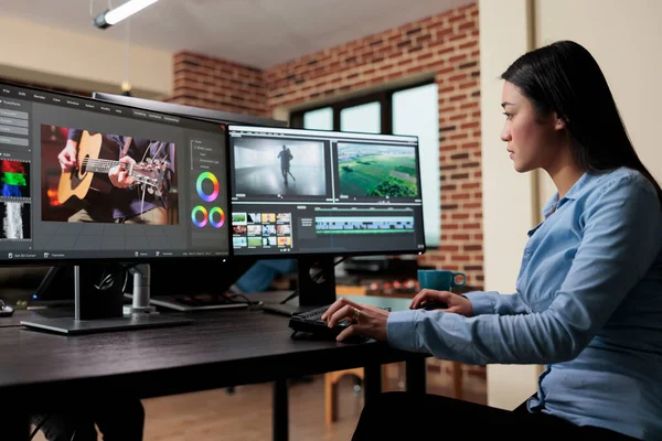 Asian professional video editor sitting at multi monitor workspace while enhancing movie — Zdjęcie stockowe