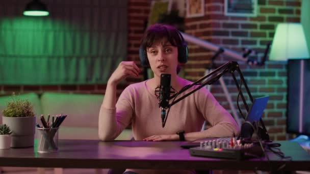 Portrait of woman with headphones smiling while streaming content from home studio sitting at desk — Wideo stockowe