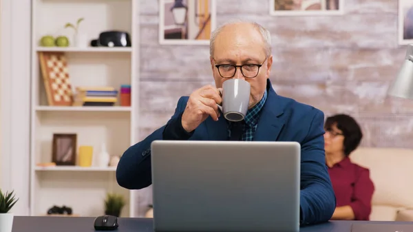 Γέρος απολαμβάνοντας ένα φλιτζάνι καφέ, ενώ εργάζονται σε φορητό υπολογιστή — Φωτογραφία Αρχείου