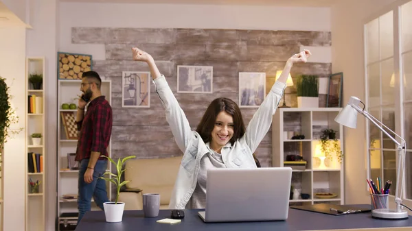Захоплена дівчина з піднятими руками під час роботи на ноутбуці у вітальні — стокове фото
