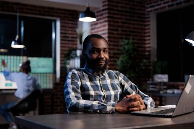 Yatırım ajansı profesyonel çalışanı ofis çalışma odasında kameraya gülümserken oturuyor..