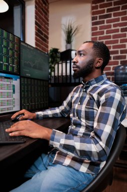 Eski borsa alım-satım acentesi gerçek zamanlı finansal verileri analiz ederken çoklu monitör çalışma istasyonuyla masada oturuyor..