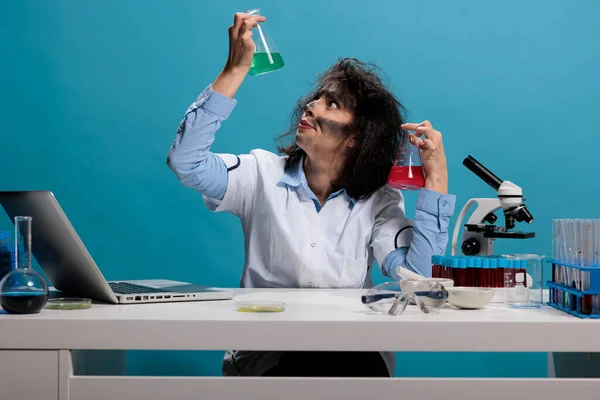 Potrait de químico tonto loco analizando frascos de prueba de vidrio llenos de sueros de experimentos líquidos mientras está sentado en el escritorio. —  Fotos de Stock