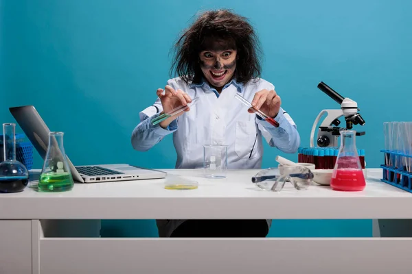 Loco experto en bioquímica tonta mezcla de compuestos químicos experimentales utilizando tubos de ensayo de vidrio mientras está sentado en el escritorio en el laboratorio. —  Fotos de Stock