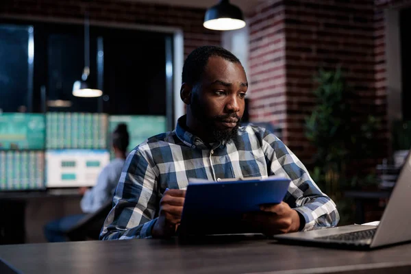 Trading agency professional employee with clipboard looking at real time market trend data charts on laptop. — Fotografia de Stock