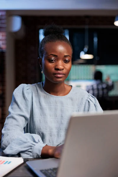 Portrait of confident african american woman sitting at desk while using laptop to do real time market analysis. — Stockfoto