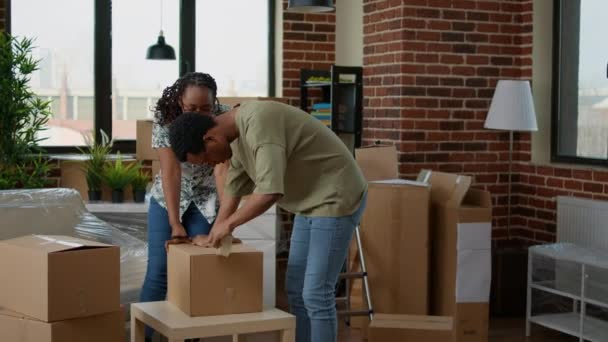 African american couple wrapping cardboard boxes with sticky tape — Stockvideo